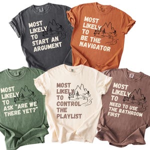 May include: Five short-sleeved t-shirts in various colors, each with a unique phrase in white text and a mountain and river graphic. The phrases include "Most Likely to Start an Argument" and "Most Likely to Be the Navigator."