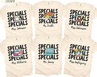 Könnte beinhalten: Sechs elfenbeinfarbene T-Shirts mit dem dreimal wiederholten schwarzen Schriftzug "SPECIALS". Jedes T-Shirt zeigt ein einzigartiges Motiv: eine Farbpalette, Sportbälle, Musiknoten, Bücherstapel, einen Laptop oder Laborbecher.