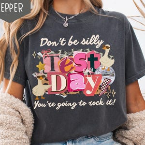 May include: Dark gray t-shirt with the text "Don't be silly Test Day You're going to rock it!" featuring cartoon geese, stars, and a disco ball. The shirt has a distressed look.