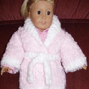 May include: A doll dressed in a pink and white plush dressing gown with a matching belt. The dressing gown has white trim around the collar and cuffs. The doll has blonde hair and a pink shirt.