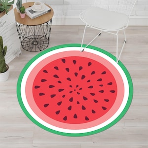 May include: A round rug with a watermelon design. The rug features a red center with black seeds, surrounded by pink, white, and green bands. The rug is on a light wood floor.