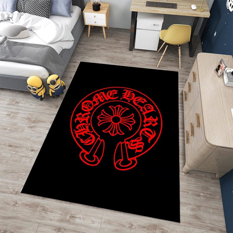May include: A rectangular area rug featuring a solid black background with a large, centered red graphic. The design consists of a circular emblem with a cross in the middle, surrounded by the text "CHROME HEARTS" in a stylized gothic font.