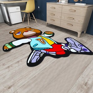 May include: A brown bear wearing a blue and yellow jacket with red pants and purple and white sneakers. The bear is laying on its back with its arms and legs outstretched. The bear is on a wooden floor.
