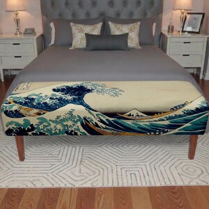 May include: A rectangular upholstered bench featuring a prominent print of The Great Wave off Kanagawa. The bench has four wooden legs and is positioned at the foot of a bed. The artwork displays deep blue waves, white foam, and tan tones.