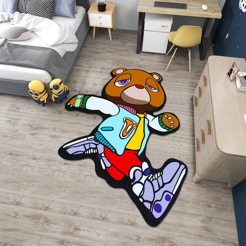 May include: A brown bear wearing a blue and yellow jacket with a red and white 'U' on the front. The bear is running and has purple and white sneakers. The bear is on a rug with a wood floor background.