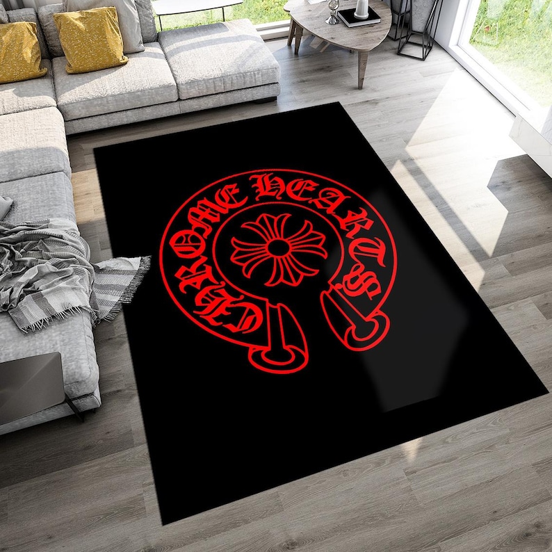 May include: A rectangular area rug featuring a solid black background with a large, centered red graphic. The design consists of a circular emblem with a cross in the middle, surrounded by the text "CHROME HEARTS" in a stylized gothic font.