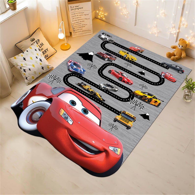 May include: A red cartoon race car with a smiling face is on a gray rug with a black race track design. The rug features other cartoon cars, including a yellow school bus, a black race car, and a blue car.