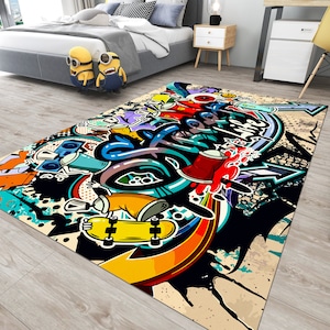 Puede incluir: Una alfombra rectangular con un vibrante dise&ntilde;o de graffiti. La alfombra presenta un monopat&iacute;n amarillo, botes de pintura en aerosol y letras en negrita en una mezcla de colores que incluyen rojo, azul y amarillo. El fondo es una mezcla de negro, beige y blanco.