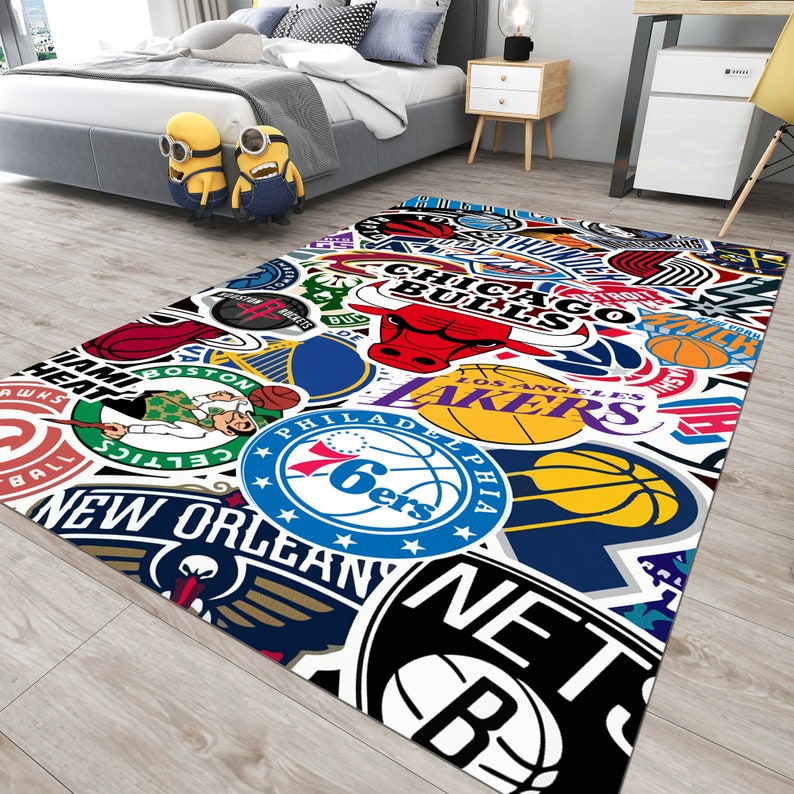 May include: A colorful rug with a white background featuring various NBA team logos, including the Chicago Bulls, Los Angeles Lakers, Philadelphia 76ers, and New Orleans Pelicans.