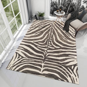 Könnte beinhalten: Ein schwarzer und weißer Zebra-Teppich mit cremefarbenem Hintergrund. Der Teppich liegt auf einem weißen Fliesenboden in einem Raum mit einem Fenster und einem Stuhl.