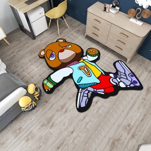 May include: A brown bear cartoon rug with a blue and yellow jacket, red pants, and purple and white sneakers. The bear is lying on its back with its arms and legs outstretched.