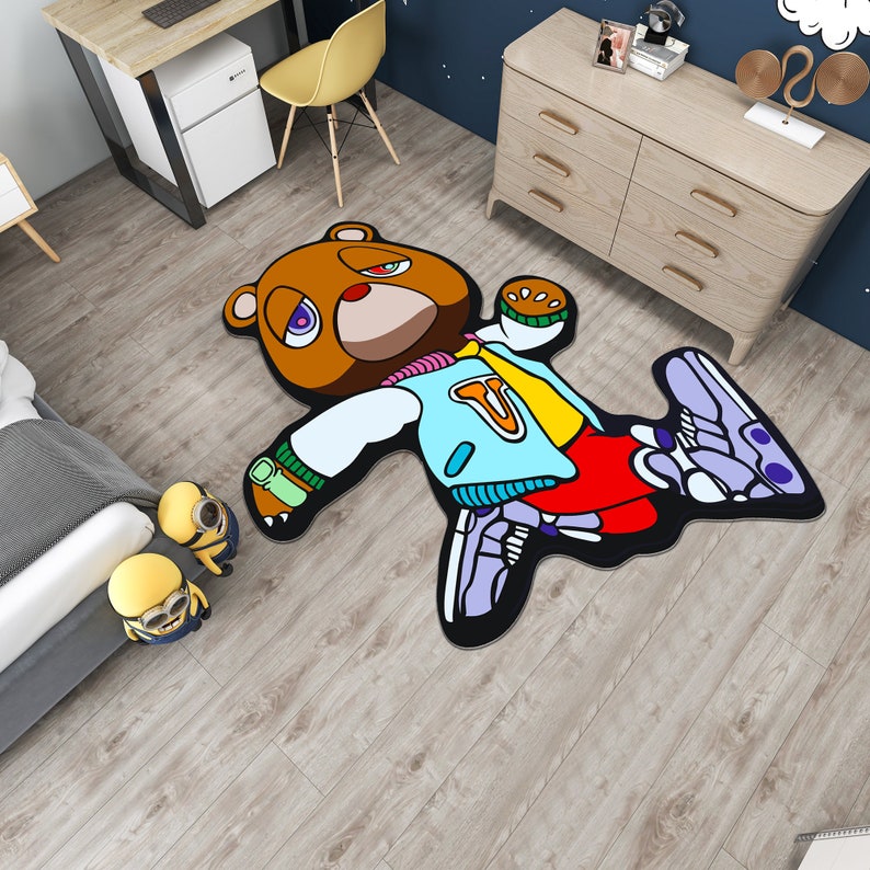 May include: A brown bear cartoon rug with a blue and yellow jacket, red pants, and purple and white sneakers. The bear is lying on its back with its arms and legs outstretched.