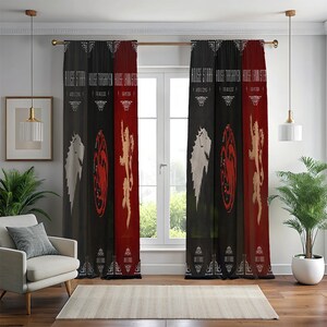 Può includere: Tende decorative per finestre con le scritte "HOUSE STARK", "HOUSE TARGARYEN" e "HOUSE LANNISTER". Ogni tenda presenta uno schema di colori diverso: nero e bianco per Stark, nero e rosso per Targaryen e rosso e oro per Lannister. Le tende sono appese davanti a una finestra.