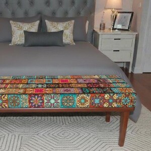 May include: A rectangular bench with four wooden legs featuring a seat upholstered in a vibrant, multi-colored fabric with a repeating pattern of intricate geometric and floral tiles in shades of blue, red, orange, yellow, and teal.