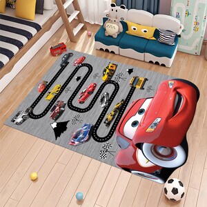 May include: A gray and black race track rug with a red cartoon car in the foreground. The rug features a black race track with white lines and checkered flags. There are several smaller cars in different colors on the track.