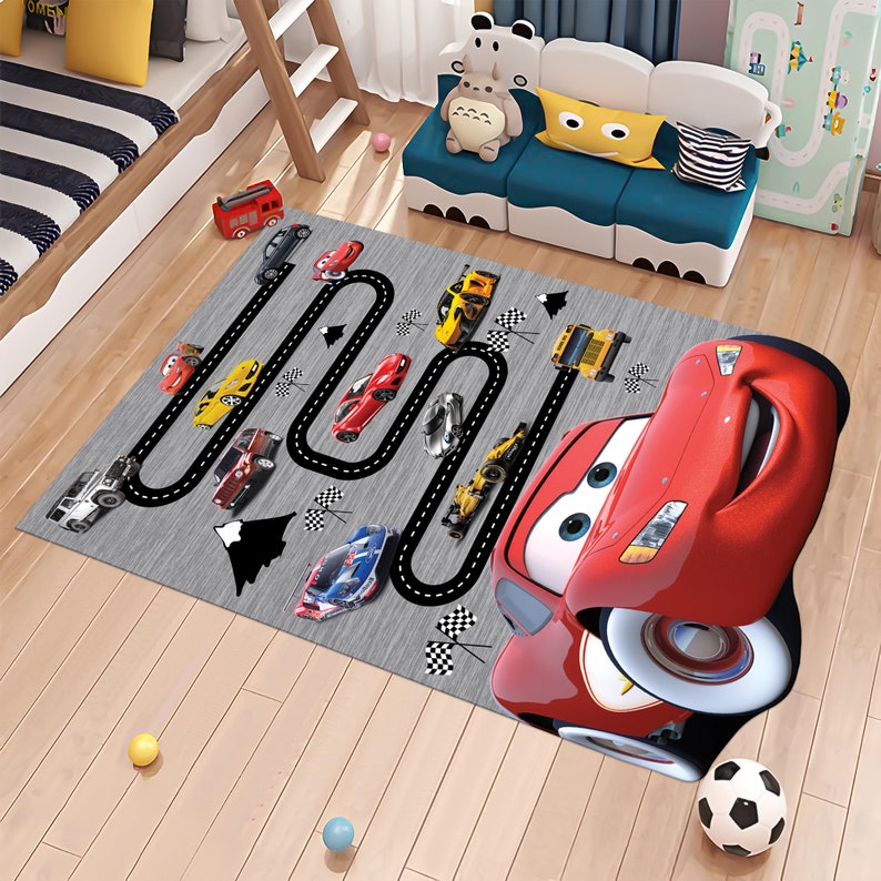 May include: A gray and black race track rug with a red cartoon car in the foreground. The rug features a black race track with white lines and checkered flags. There are several smaller cars in different colors on the track.