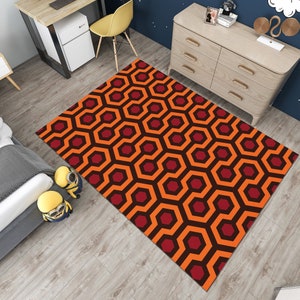 May include: A geometric patterned rug with orange and red hexagons. The rug has a black outline around each hexagon. The rug is on a wooden floor.