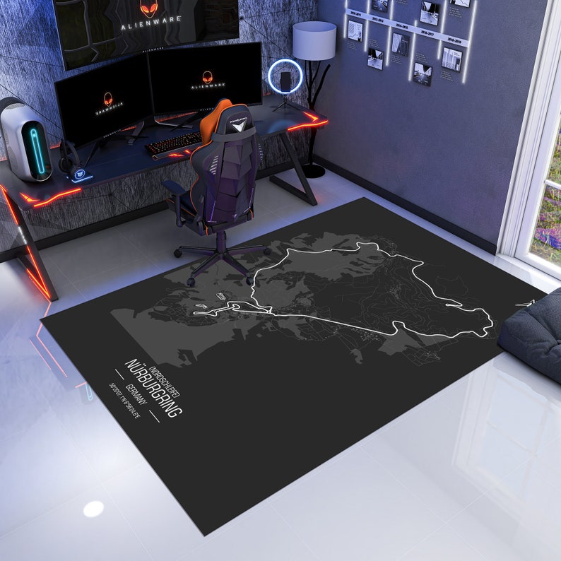 May include: A black and white map of the N&uuml;rburgring race track on a black rug. The rug is in a room with a gaming setup, including a desk, two computer monitors, a gaming chair, and a white tower computer.