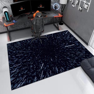 Puede incluir: Una alfombra rectangular con un fondo azul oscuro y un patrón de explosión estelar blanco. La alfombra está colocada en una habitación con una configuración de juego, que incluye un escritorio, una silla y dos monitores.