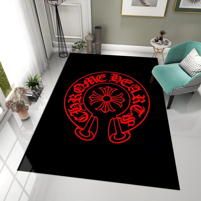 May include: A rectangular area rug featuring a solid black background with a large, centered red graphic. The design consists of a circular emblem with a cross in the middle, surrounded by the text "CHROME HEARTS" in a stylized gothic font.