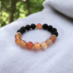 Può includere: Un braccialetto realizzato con pietre di lava nera e perle di cornalina. Il braccialetto presenta un effetto sfumato, con le perle di cornalina che vanno dal color arancio chiaro al color arancio scuro.
