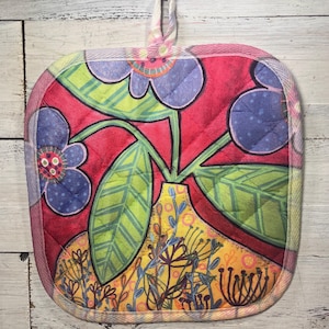 May include: Square quilted potholder with a colorful floral design. The potholder features a red background with blue flowers, green leaves, and a yellow vase. It has a loop for hanging and a patterned border.