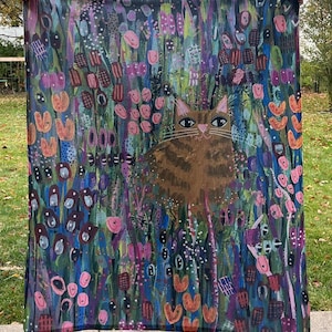 May include: A colorful throw blanket with a brown cat in the center. The cat is surrounded by a variety of flowers and plants in shades of pink, blue, green, and purple.