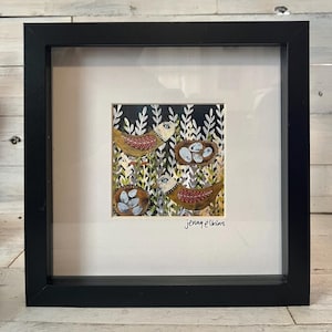 May include: Framed artwork featuring two birds and two nests with eggs, set against a backdrop of stylized foliage. The birds are brown with red wing details. The artwork is signed "jenny elkins". The frame is black.