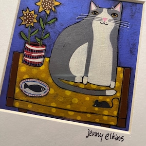May include: A framed painting of a gray and white cat sitting on a yellow dotted surface. Two sunflowers in a red and white striped vase are to the left of the cat. A black mouse and a fish-shaped design are also on the surface. The artist's signature, "jenny elkins", is in the bottom right corner.