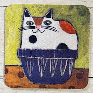 May include: Square coaster featuring a whimsical cat illustration. The cat is white with black and orange markings, sitting in a blue container against a yellow and orange background. The coaster has a playful, artistic design.