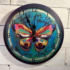 May include: Round wall clock with a colorful butterfly design. The clock face is blue and green with the words "fight for the things you care about." Black clock hands and a red second hand complete the design.