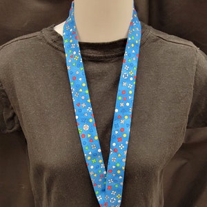 May include: A blue lanyard with a colorful pattern of geometric shapes and symbols. The lanyard is made of fabric and has a black metal clip.