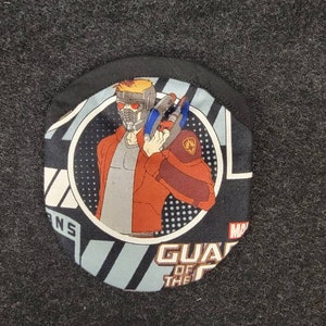 May include: A black and white fabric patch with a cartoon image of Star-Lord from Guardians of the Galaxy. The patch features the text "Guardians of the Galaxy" and the Marvel logo.