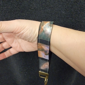 May include: A black and white key chain with a colorful galaxy print. The key chain has a gold metal ring and a gold metal clasp.