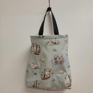 May include: A light blue tote bag with black handles and a nautical print featuring ships, islands, and buildings.