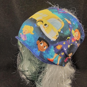 May include: A blue and white patterned hat featuring cartoon characters and a yellow school bus against a starry background. The hat has a blue trim and is made of a soft fabric.