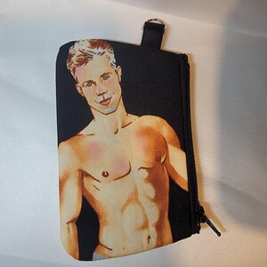 May include: Black zippered pouch featuring a stylized illustration of a shirtless person with light skin, blonde hair, and blue eyes. The pouch has a black strap and a silver ring attached. The background is black.