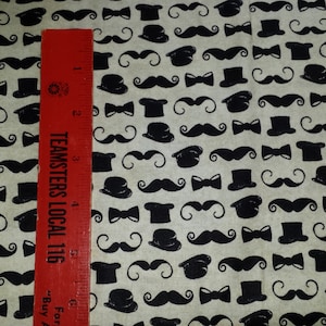May include: Cream-colored fabric with a repeating pattern of black mustaches, bow ties, and top hats. A red ruler with white text is placed vertically on the fabric, showing measurements in inches. The text on the ruler reads "TEAMSTERS LOCAL 116".