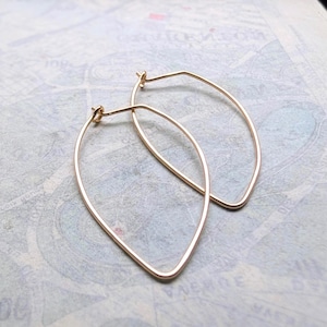 May include: A pair of gold-toned hoop earrings featuring a distinct marquise or leaf-like shape. The earrings are constructed from thin, smooth wire that tapers to a point at the bottom and includes a simple hook closure mechanism at the top.