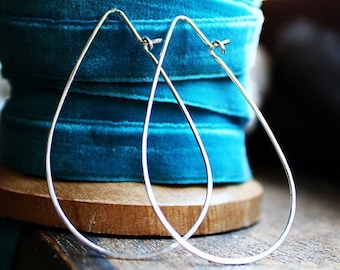 May include: A pair of silver teardrop-shaped hoop earrings. The earrings are hanging from a spool of teal blue velvet ribbon.