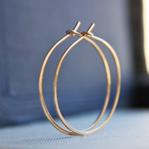 May include: A pair of gold hoop earrings. The hoops are thin and delicate, and they are made of a smooth, shiny metal.