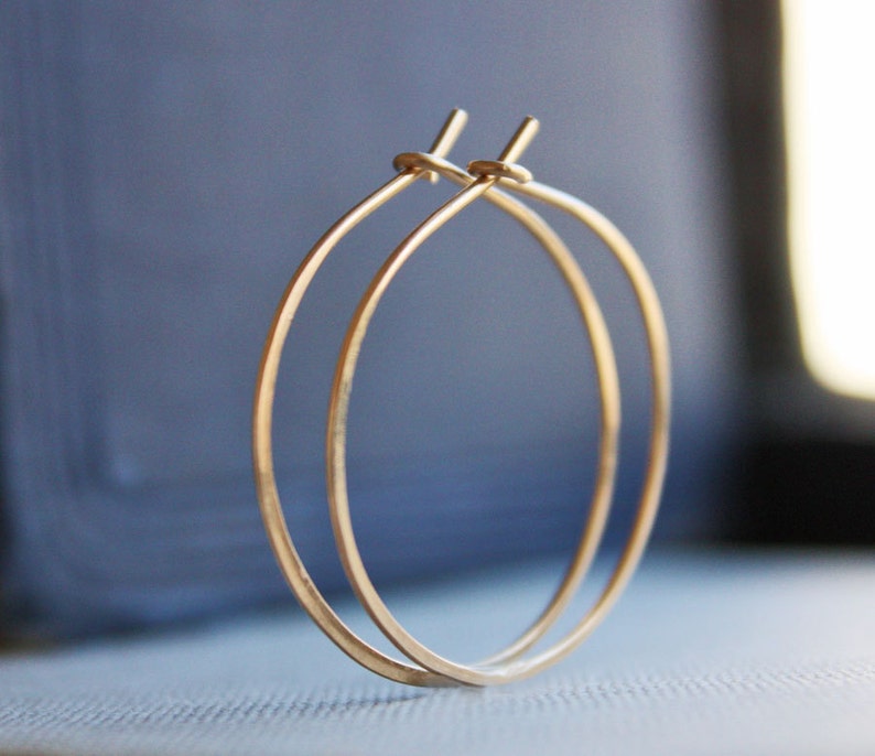 May include: A pair of gold hoop earrings. The hoops are thin and delicate, and they are made of a smooth, shiny metal.