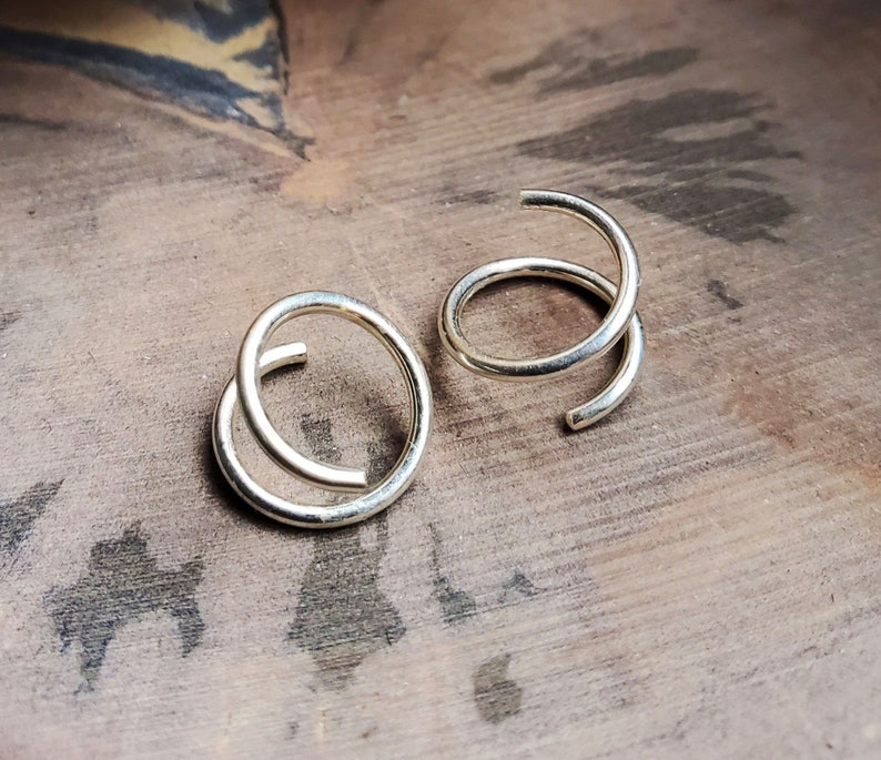 May include: Two silver hoop earrings, each with a double-loop design. The earrings are on a wooden surface.