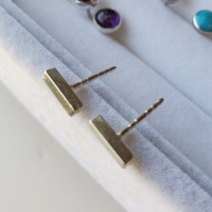 May include: Two silver bar earrings with a textured finish. The earrings are on a white background.