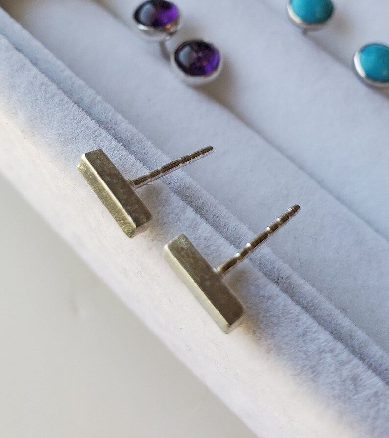 May include: Two silver bar earrings with a textured finish. The earrings are on a white background.
