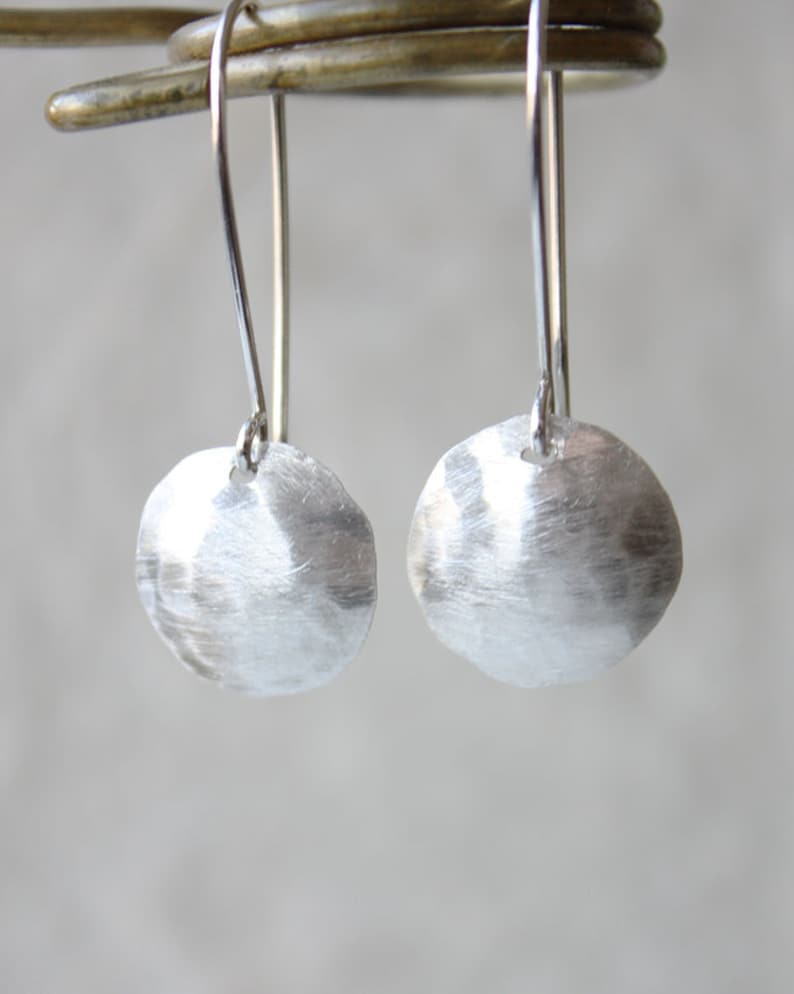 May include: A pair of silver dangle earrings with hammered round discs. The earrings have a simple, minimalist design.
