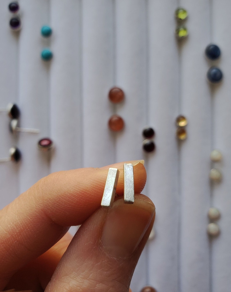 May include: A pair of silver bar stud earrings. The earrings are small and simple, and they are perfect for everyday wear.