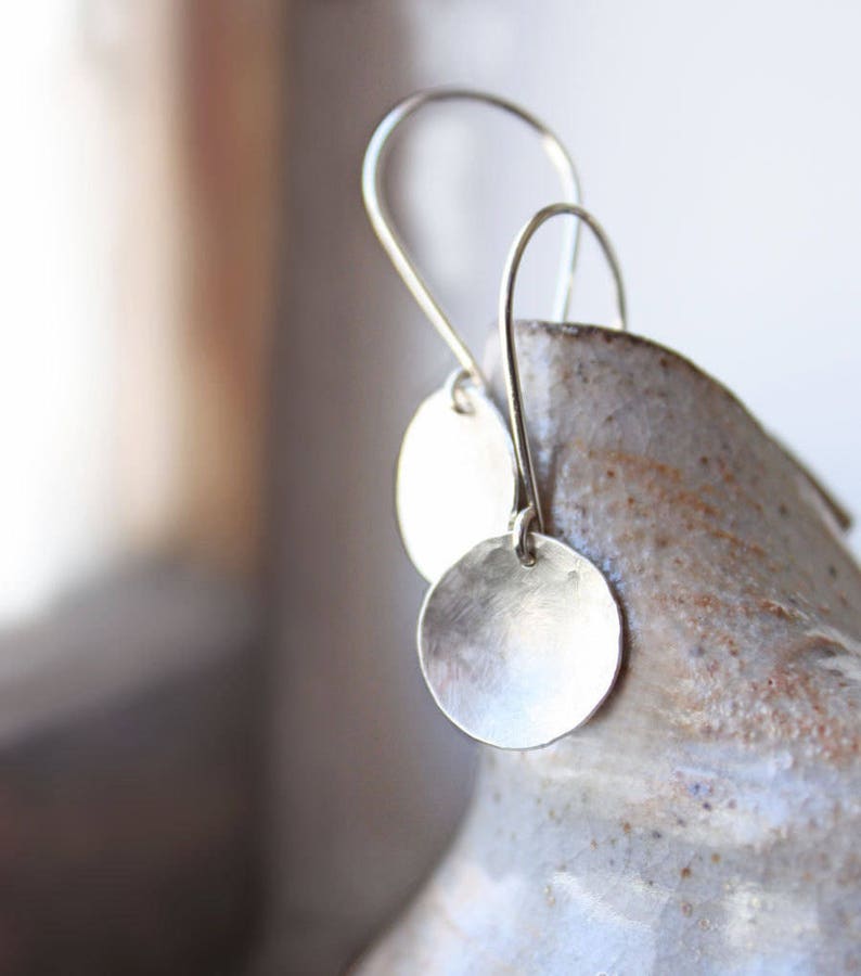 May include: A pair of silver dangle earrings with a hammered, circular disc pendant. The earrings are hanging from a simple hook.