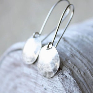 May include: Silver dangle earrings with hammered round disc charms. The earrings have a simple, minimalist design.