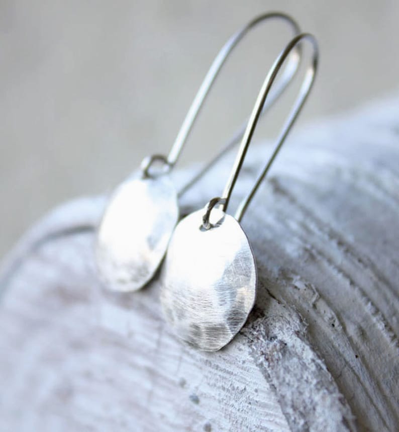 May include: Silver dangle earrings with hammered round disc charms. The earrings have a simple, minimalist design.